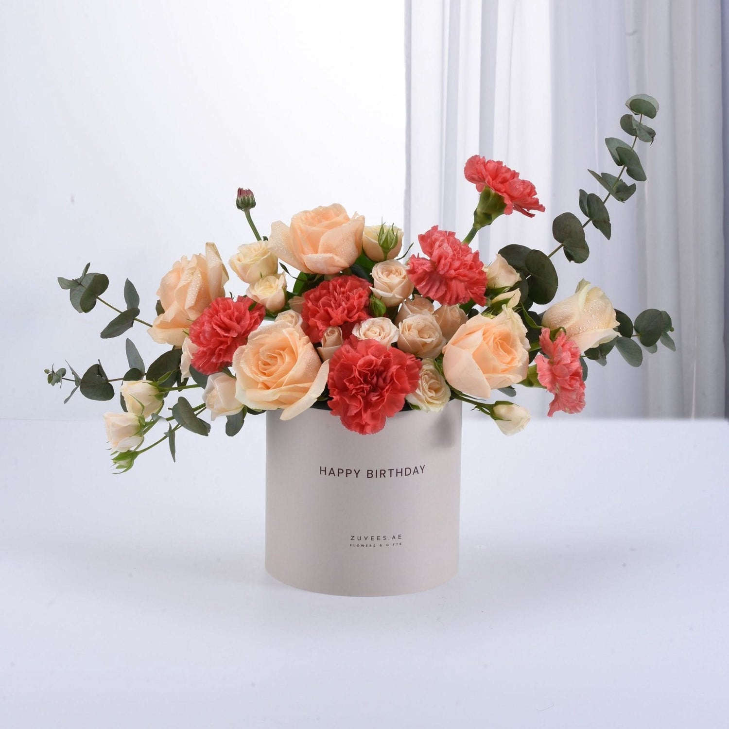 Soft peach roses and coral carnations in minimalist beige birthday box.