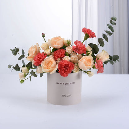 Soft peach roses and coral carnations in minimalist beige birthday box.