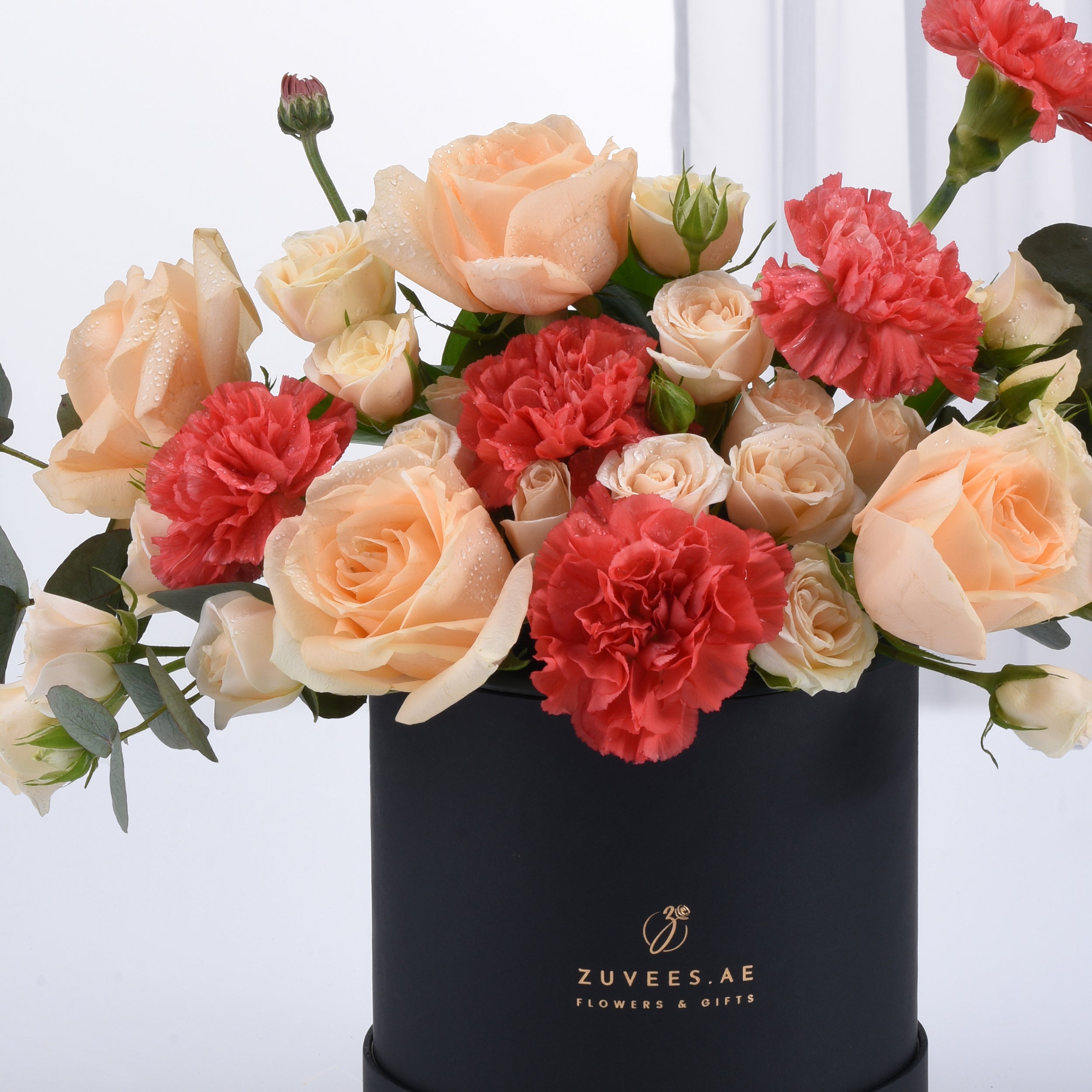 Peach roses, coral carnations, dew-kissed petals in sleek black Zuvees gift box.