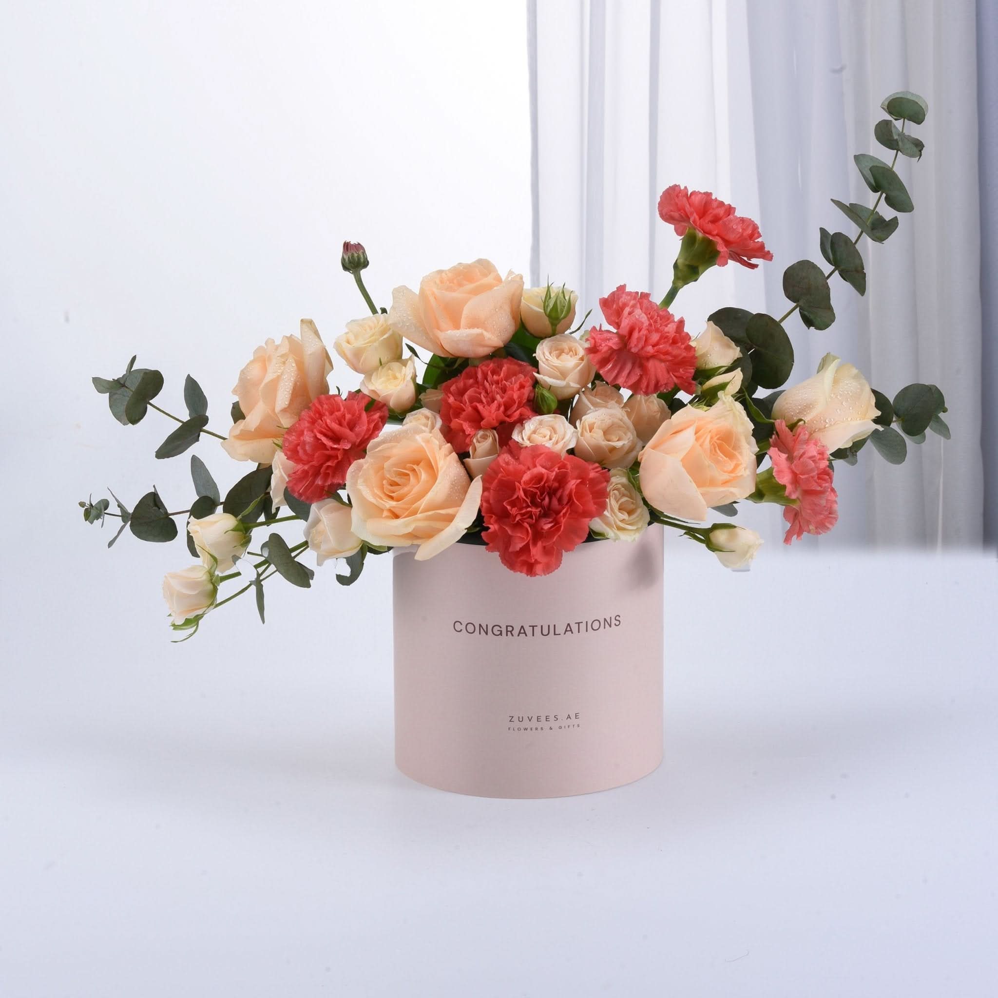 Soft pink box holds peach roses and coral carnations, eucalyptus accents.