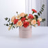 Soft pink box holds peach roses and coral carnations, eucalyptus accents.