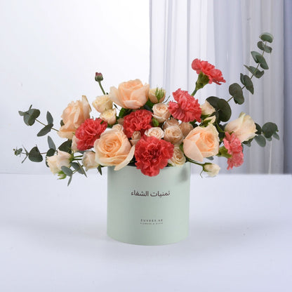 Pastel peach roses and coral carnations in mint-green cylindrical vase.