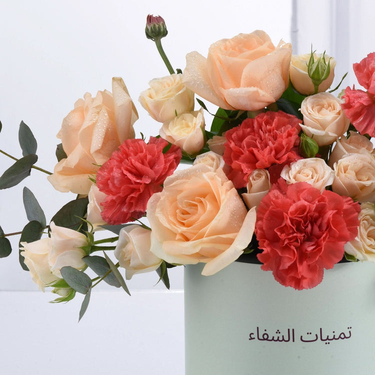 Peach roses, red carnations, eucalyptus in mint vase, dew-kissed, elegant floral arrangement.