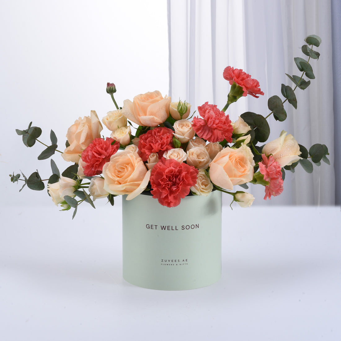 Pastel peach roses and coral carnations in mint box with "Get Well Soon" message.