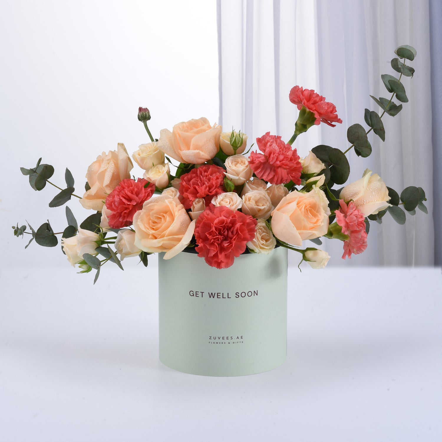 Pastel peach roses and coral carnations in mint box with "Get Well Soon" message.