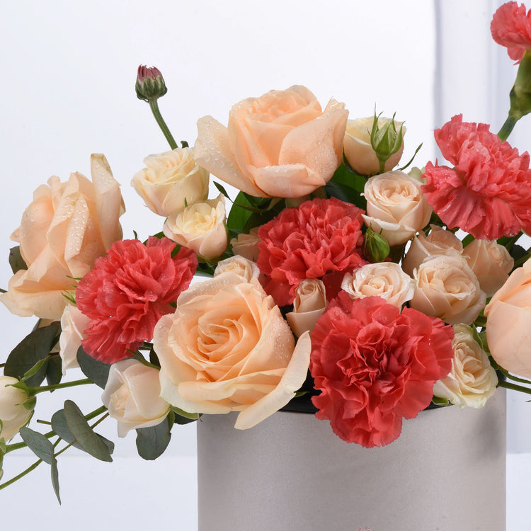 Soft peach roses and coral carnations glisten with dew in sleek silver vase.