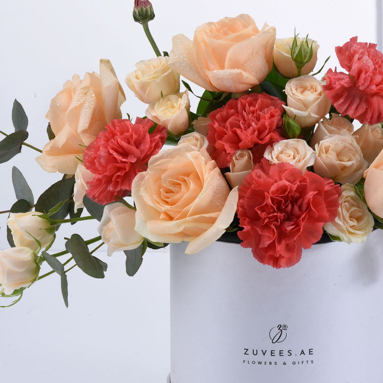 Soft peach roses and coral carnations with dewdrops in white box.