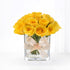 Vibrant yellow roses in clear glass vase, elegantly tied with branded beige ribbon.