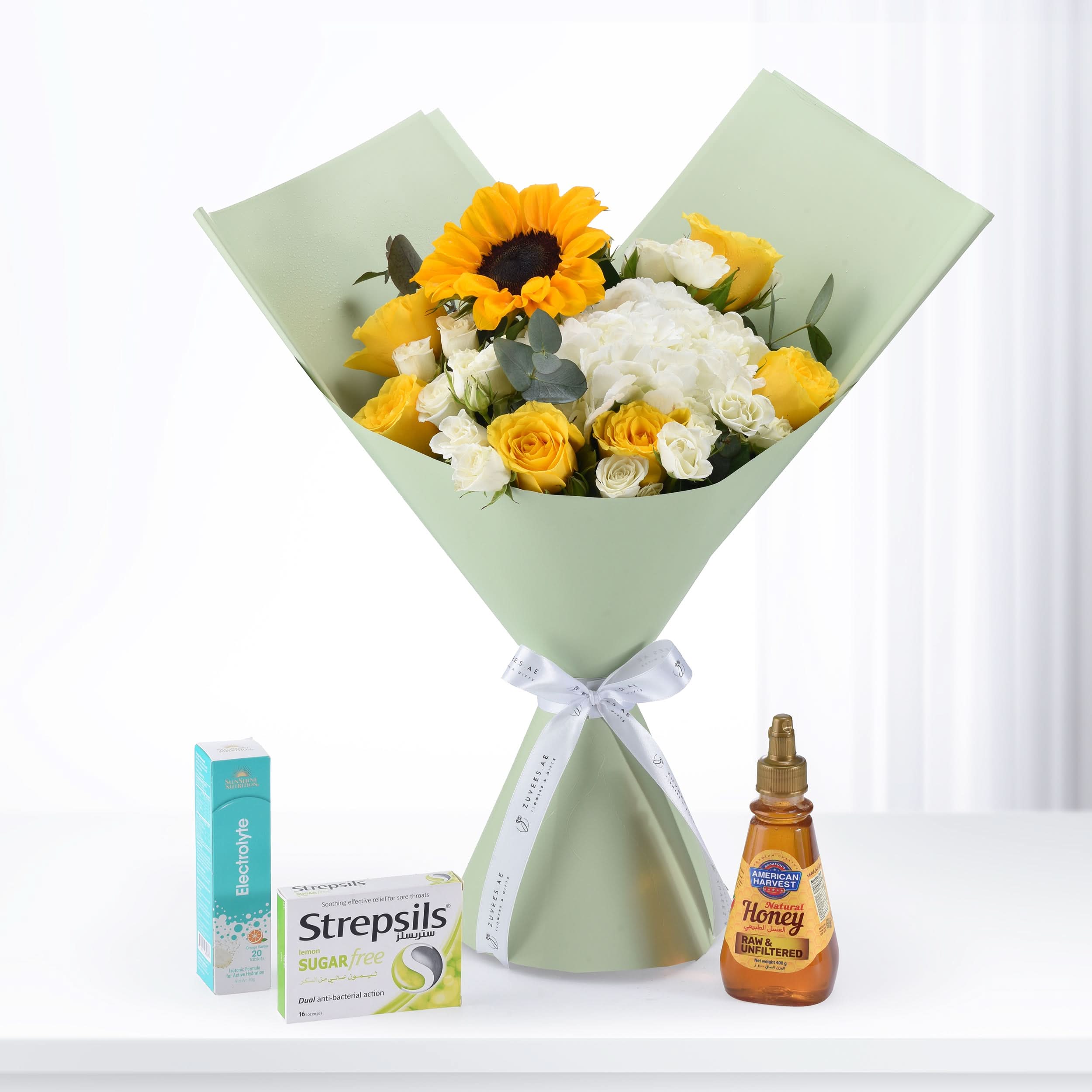 Sunflower and rose bouquet wrapped in sage green paper, with honey, Strepsils, and electrolyte.