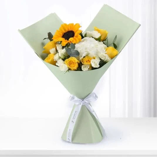 Vibrant sunflower and rose bouquet in mint paper, tied with white ribbon.