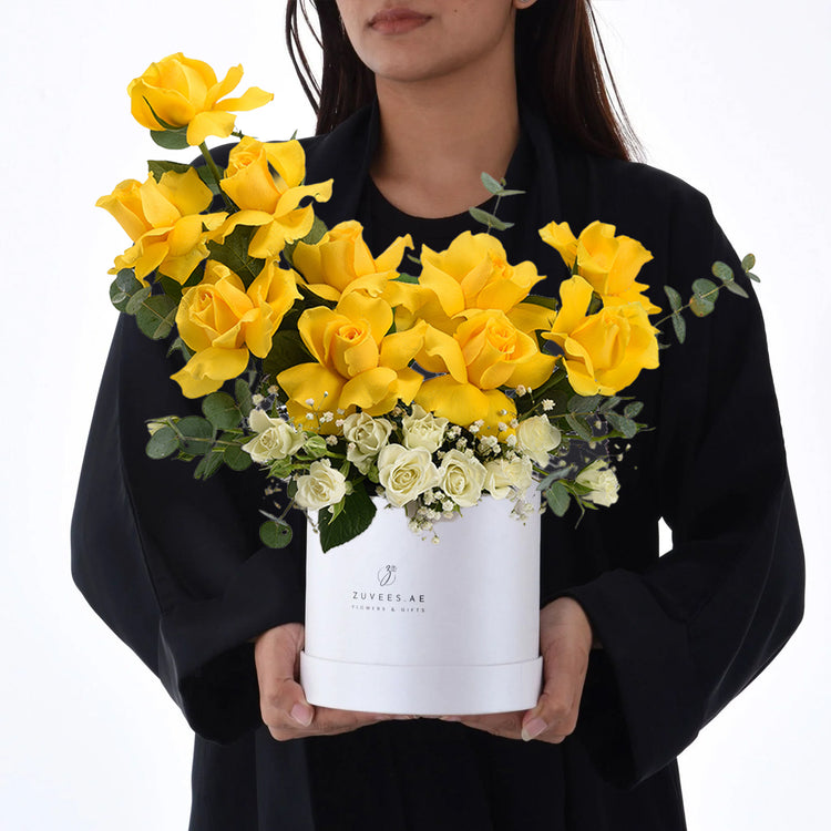 Vibrant yellow roses and white blooms in elegant white box held by person.
