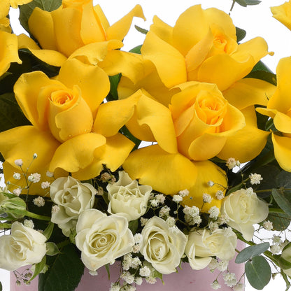 Vibrant yellow and white roses with dewdrops, accented by baby’s breath in a soft pink vase.