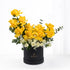 Vibrant yellow roses and white blooms elegantly arranged in a sleek black cylindrical box.