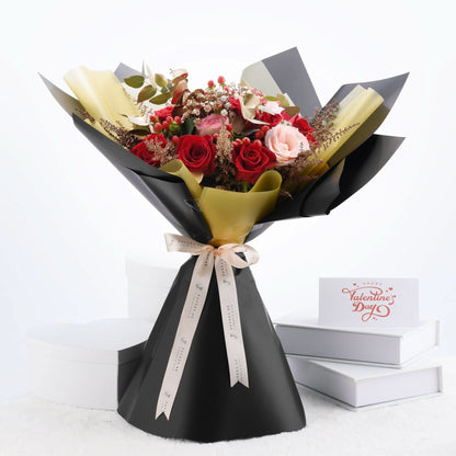 Elegant Valentine’s bouquet with red and pink roses, gold accents, and black wrapping.