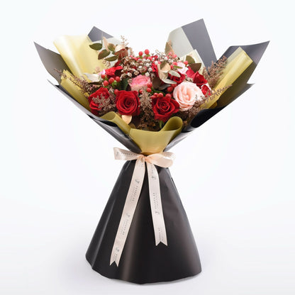 Elegant bouquet with red and pink roses, gold accents, and black wrapping.