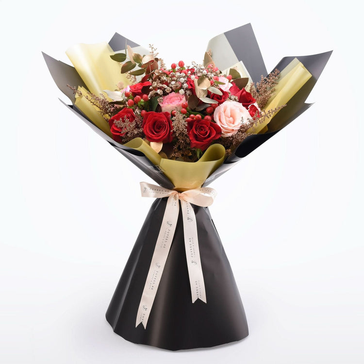 Elegant bouquet with red and pink roses, gold accents, and black wrapping.