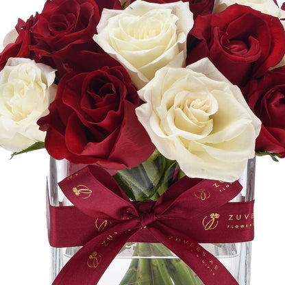 Luxurious red and white roses in clear vase, tied with burgundy ribbon featuring gold logo.