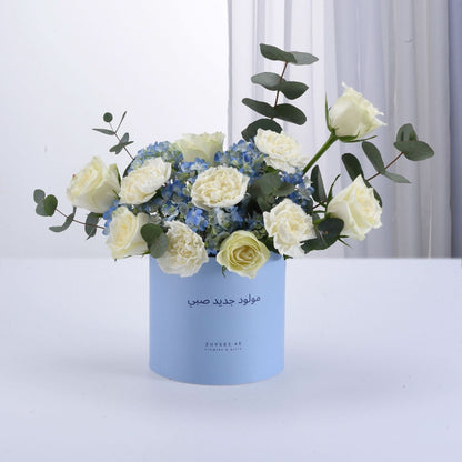 Light blue box holds white roses and blue hydrangeas with eucalyptus.