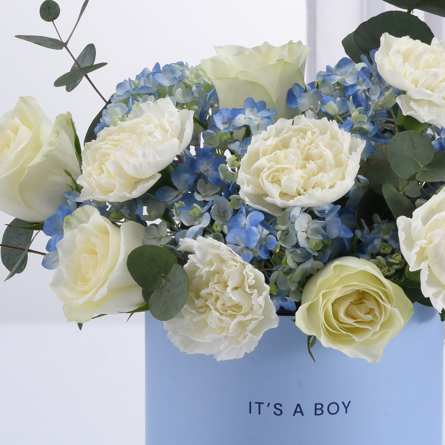 Elegant baby blue vase holds creamy white roses and hydrangeas for boy celebration.