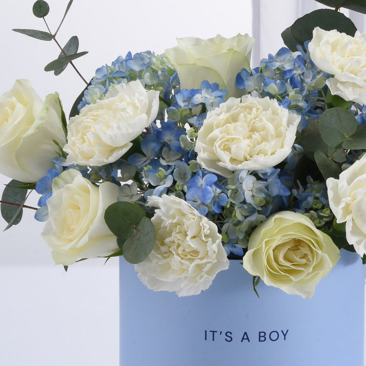Elegant baby blue vase holds creamy white roses and hydrangeas for boy celebration.