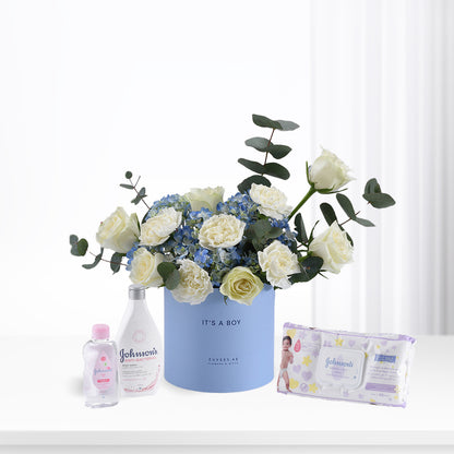 Soft blue floral arrangement with white roses and hydrangeas, paired with Johnson’s baby essentials for a boy.