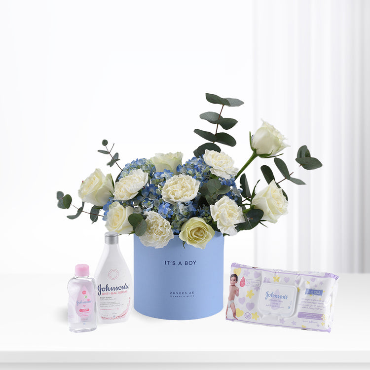 Soft blue floral arrangement with white roses and hydrangeas, paired with Johnson’s baby essentials for a boy.