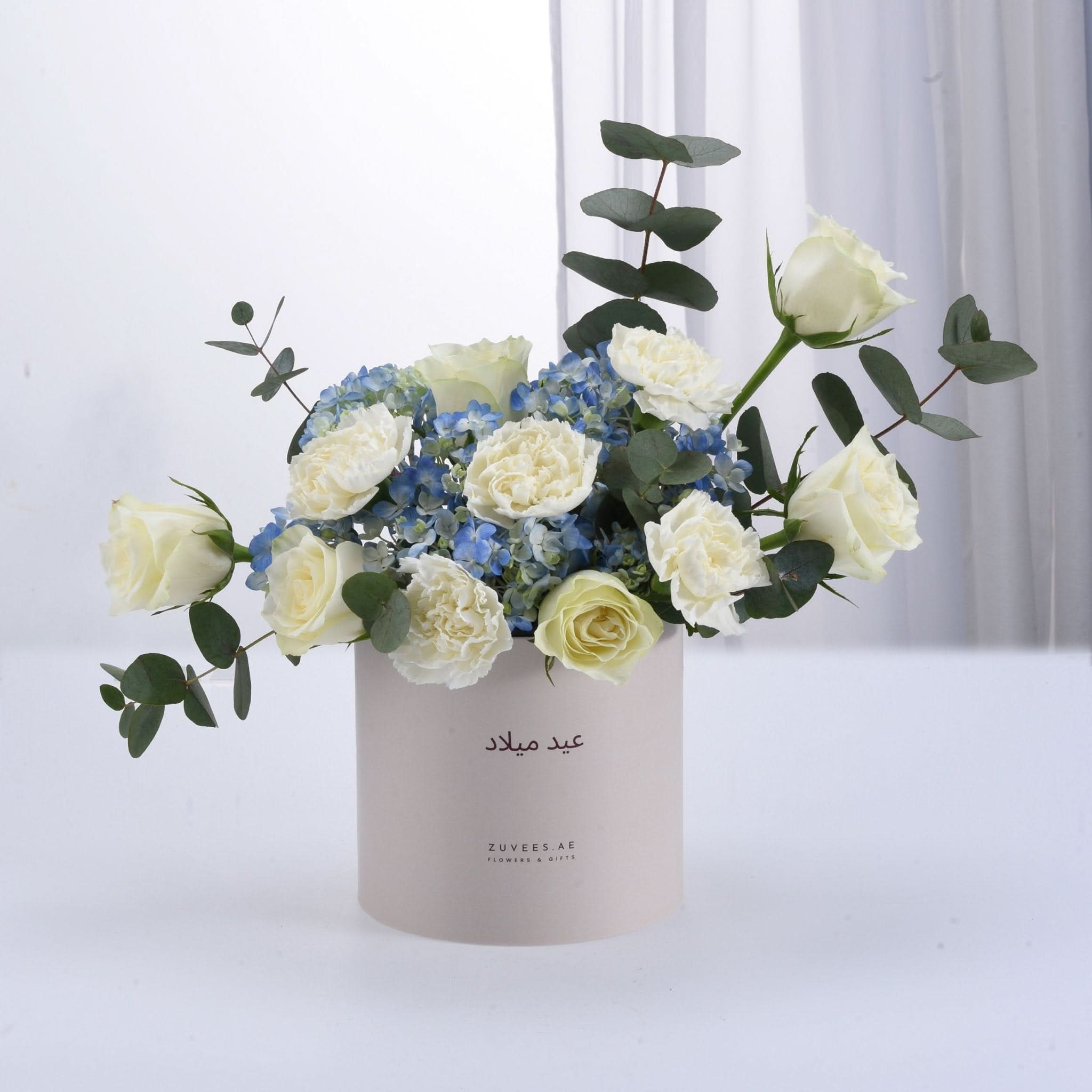 Elegant white roses and blue hydrangeas in minimalist beige box.