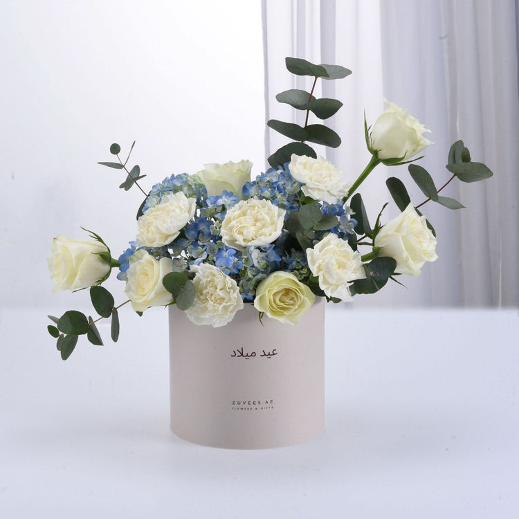 Elegant white roses and blue hydrangeas in minimalist beige box.