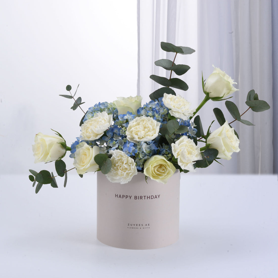 White roses, blue hydrangeas, eucalyptus in "Happy Birthday" vase, elegant gift arrangement.