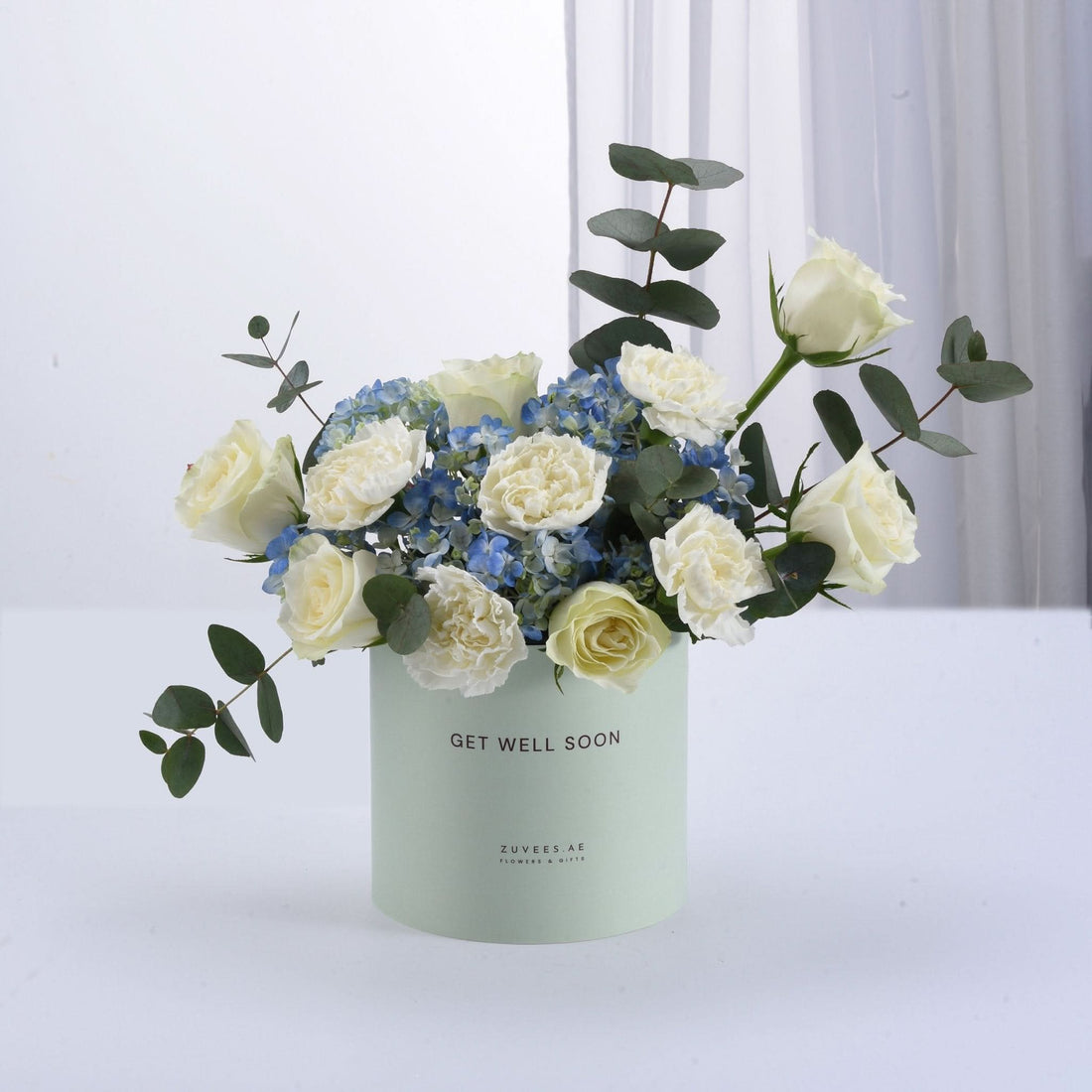 Pastel green box holds white roses and blue hydrangeas, “Get Well Soon” message.