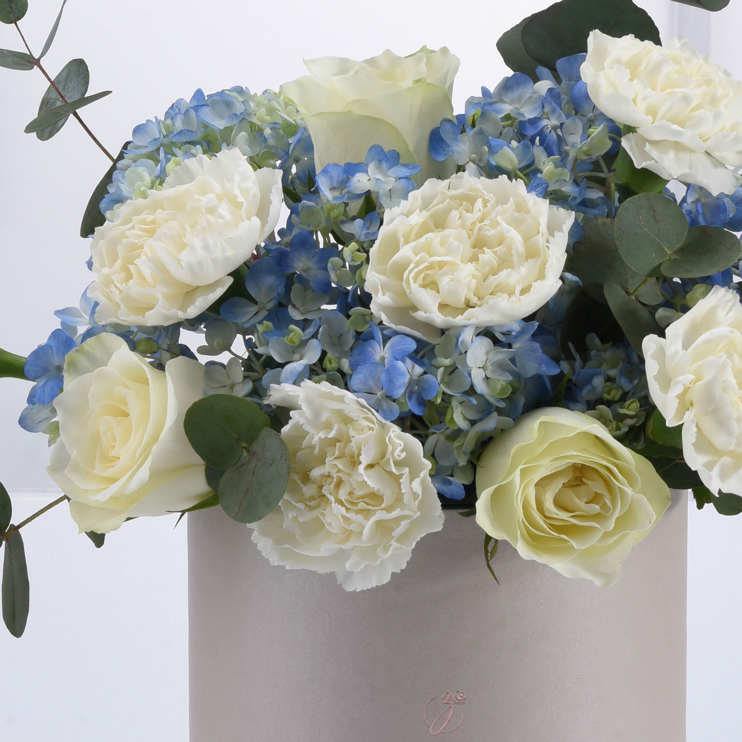 Elegant white roses, blue hydrangeas, and eucalyptus in matte gray vase.
