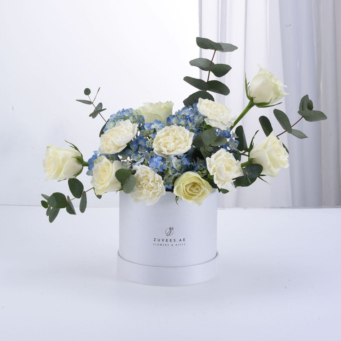 White roses and blue hydrangeas in elegant white box with eucalyptus.