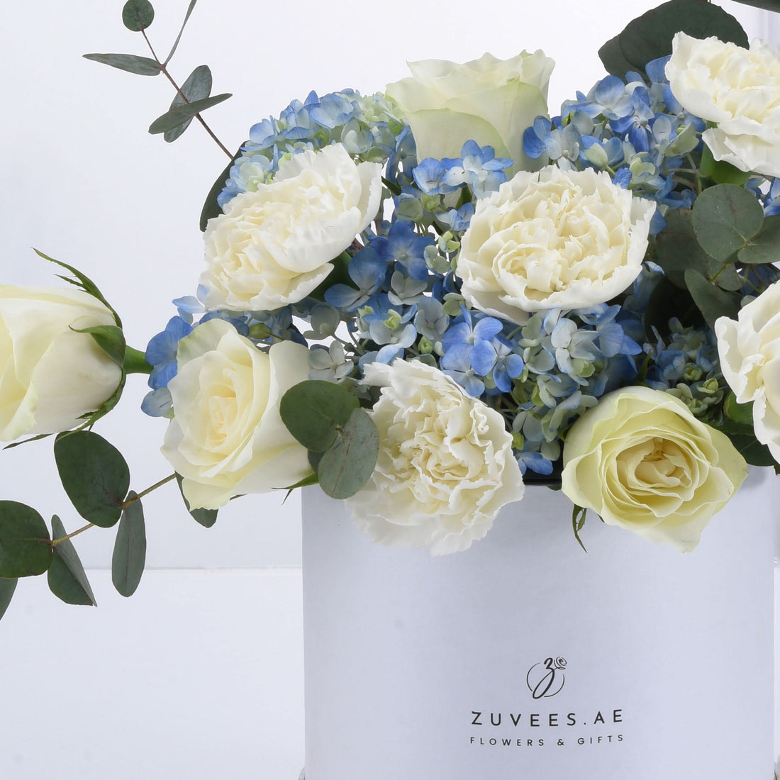 Elegant white roses, peonies, and blue hydrangeas in minimalist white box.