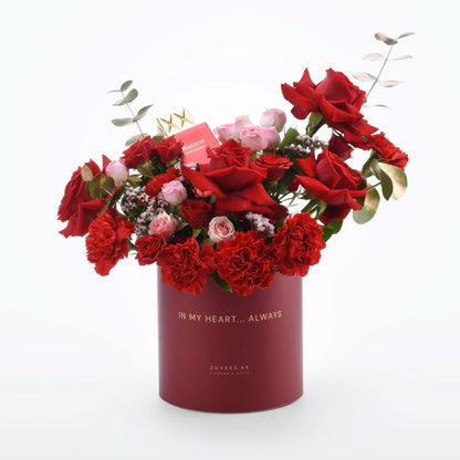 Vibrant red roses and carnations in elegant maroon cylinder with gold text.