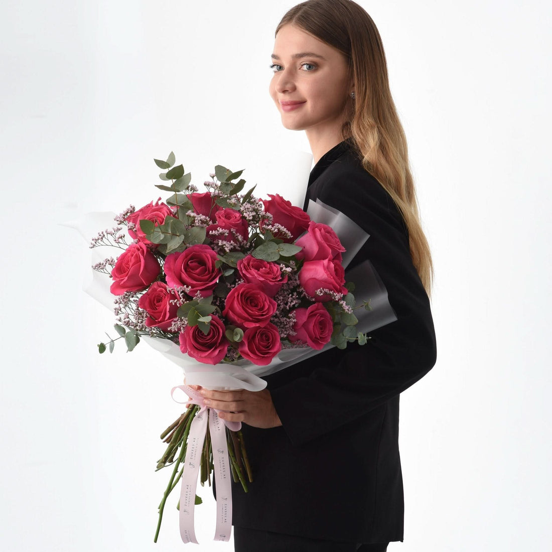 Vibrant pink roses with eucalyptus, wrapped in white paper, held by woman in black blazer.