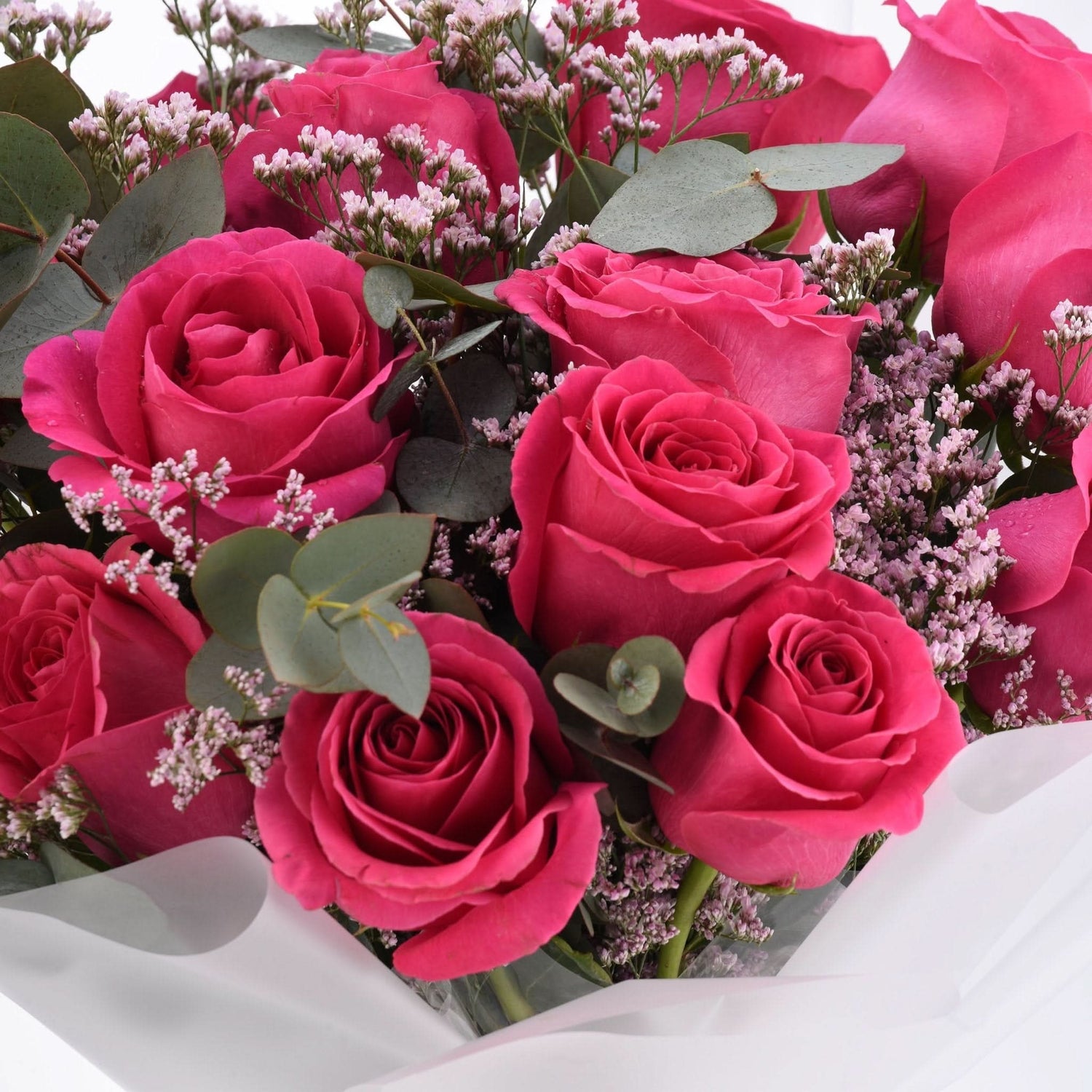 Vibrant pink roses nestled with baby’s breath and eucalyptus in white wrap.