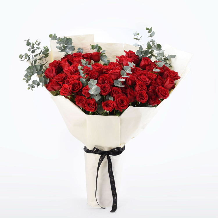 Vibrant red roses with eucalyptus, wrapped in cream paper and black ribbon.