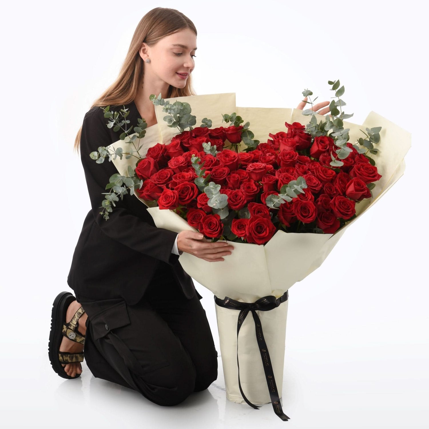 Woman kneels, admiring large bouquet of vibrant red roses with eucalyptus.