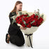 Woman kneels, admiring large bouquet of vibrant red roses with eucalyptus.
