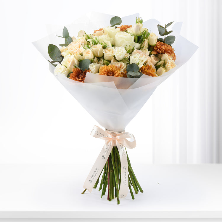 Cream roses and orange gerberas wrapped in white paper with branded ribbon.
