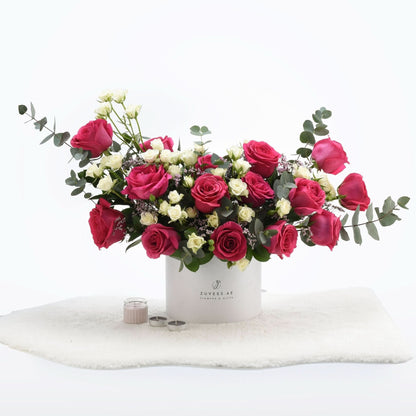 Vibrant pink and white roses in sleek white box, accented with eucalyptus and candles.