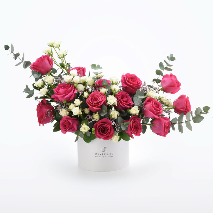 Vibrant pink and white roses with eucalyptus in a branded white cylindrical box.