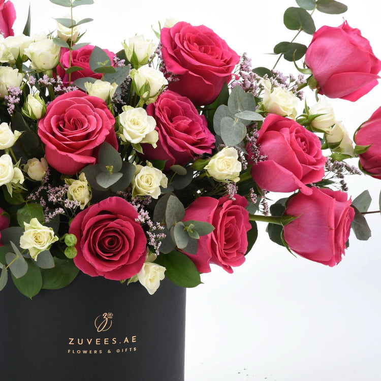 Vibrant pink and white roses with eucalyptus in sleek black vase.