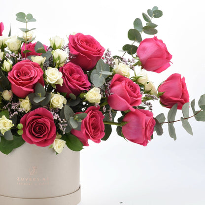 Vibrant pink and white roses cascade from beige box, accented with eucalyptus.