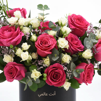 Vibrant pink and white roses with eucalyptus, dew-kissed, in sleek black vase, Arabic text "أنت عالمي".