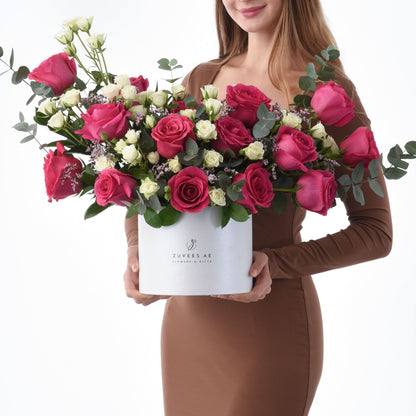 Vibrant pink and white roses with eucalyptus in sleek white Zuvees box, held by woman in brown dress.