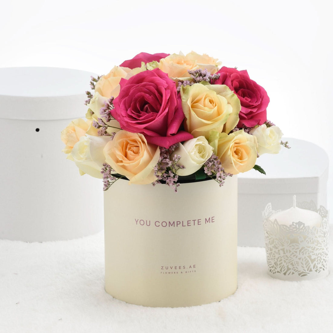 Cream box holds vibrant pink, peach, and white roses with lavender accents.