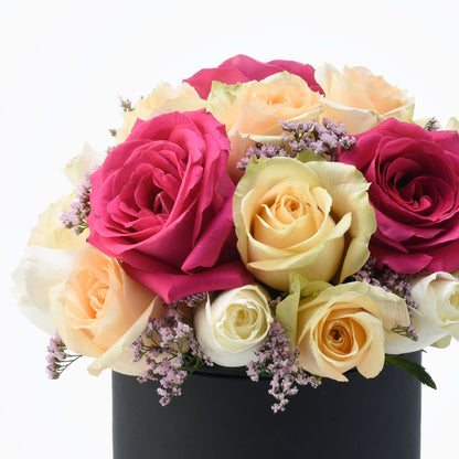 Vibrant pink, peach, and white roses with purple filler blooms in a sleek black box.