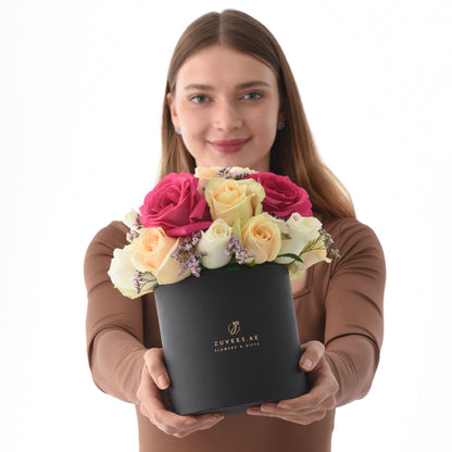 Woman holds elegant black box of vibrant pink, yellow, and white roses with lavender accents.