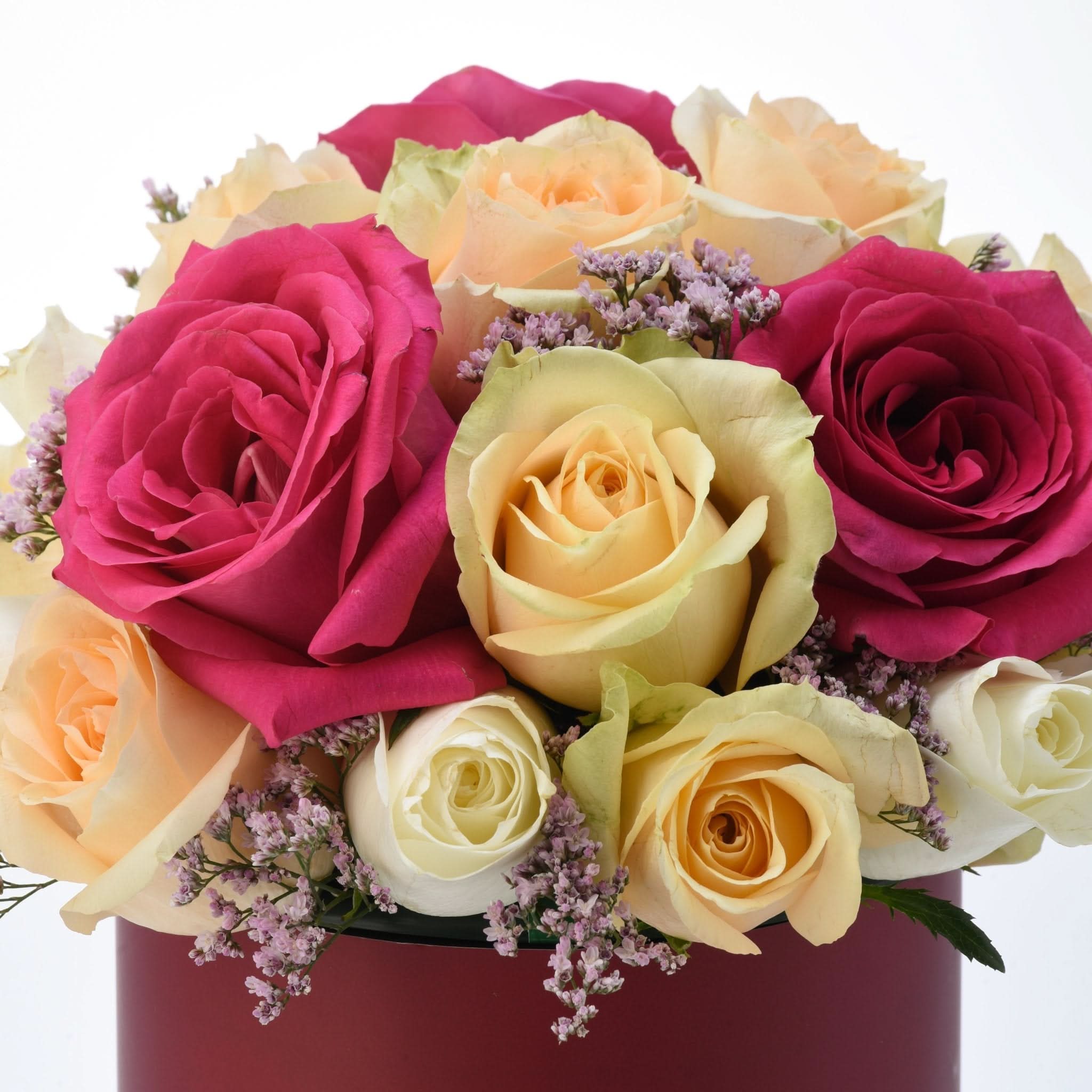 Vibrant pink, yellow, white roses with purple filler blooms in deep red box, lush and romantic.
